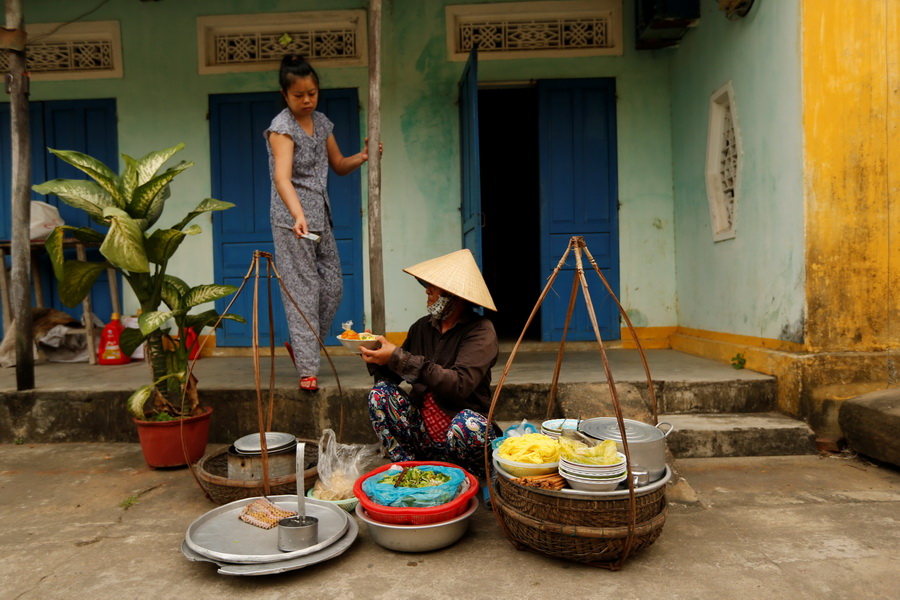 A woman wearing a traditional hat, known as a non la, sells food for breakfast in Hoi An, Vietnam April 5, 2016.