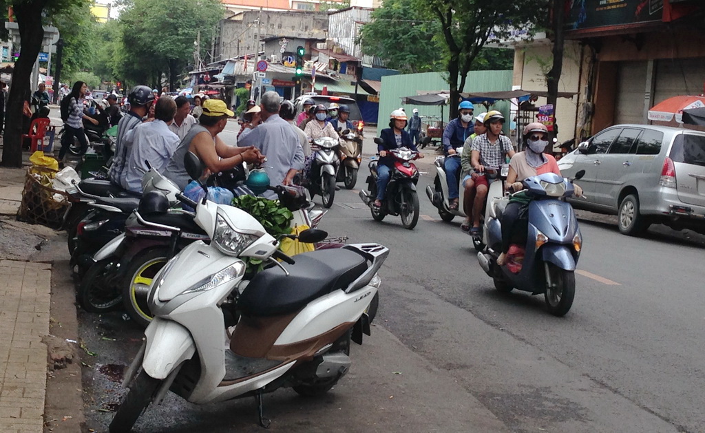 Bikes are parked along the street with riders sitting on them. Photo: Tuoi Tre