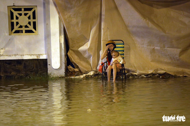 A mother and child wait in the flood water while their motorbike gets fixed. Photo: Tuoi Tre