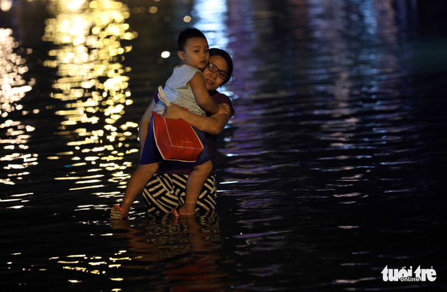 A mother and child wade through waist-deep floodwater. Photo: Tuoi Tre