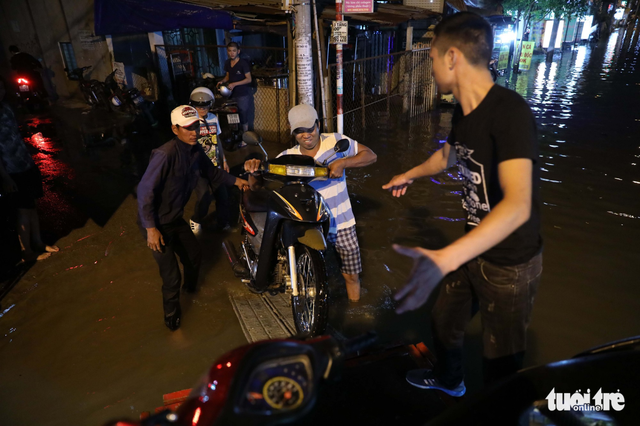 Motorbikes are loaded onto a motorized cyclo to be transport through a flooded street. Photo: Tuoi Tre