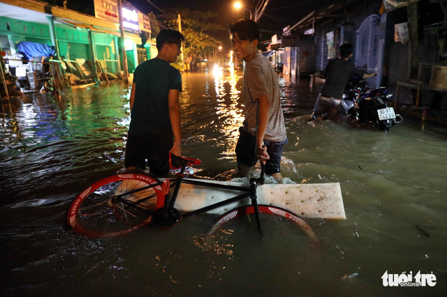 Two men put their bicycle on a float to pull it through the floodwater. Photo: Tuoi Tre