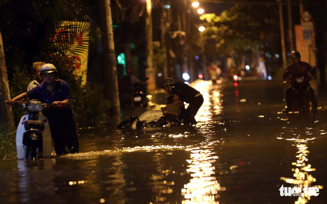 Commuters push their vehicles through floodwater. Photo: Tuoi Tre