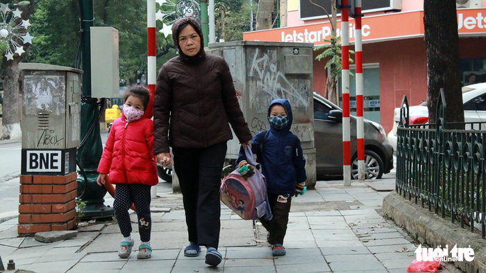 A woman walks her two children to school.