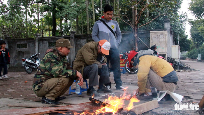 A group of motorbike taxi drivers sit by a bonfire on Kim Ma Street.
