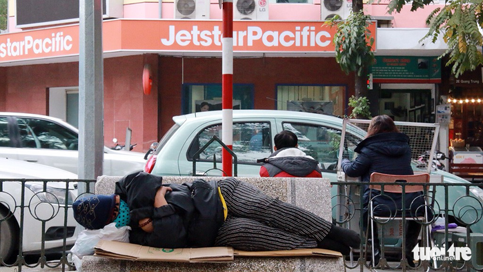 A homeless person sleeps on a bench on a sidewalk.