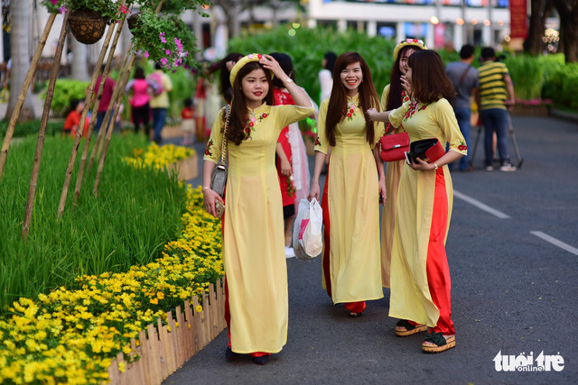 A group of young women wearing Vietnam ao dai takes a walk along a flower-lined street in Phu My Hung. Photo: Tuoi Tre