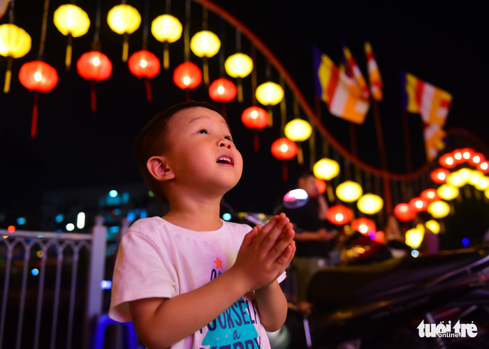 A little boy prays in the background of many brightly-colored lanterns. Photo: Tuoi Tre