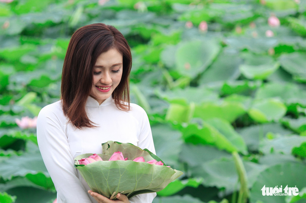 A girl in ao dai poses with lotus flowers in Hanoi. Photo: Tuoi Tre