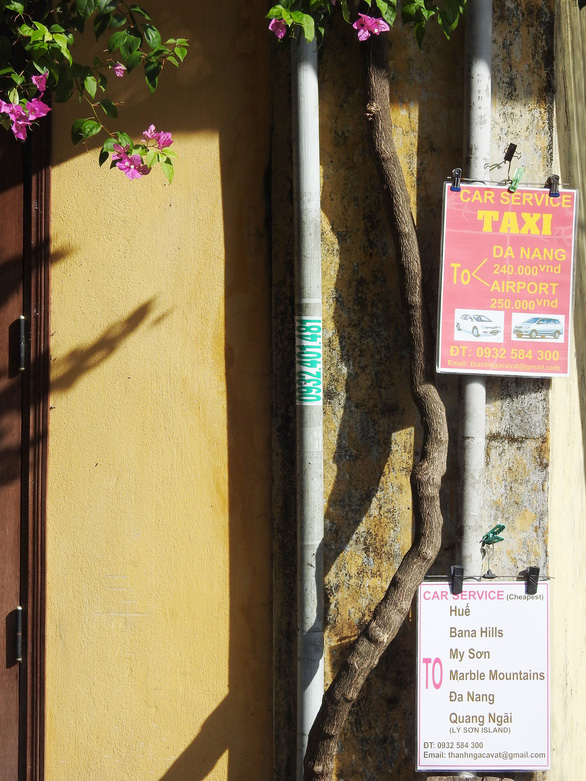 Banners and signboards belonging to private businesses cover a yellow wall in the ancient town. Photo: Tuoi Tre