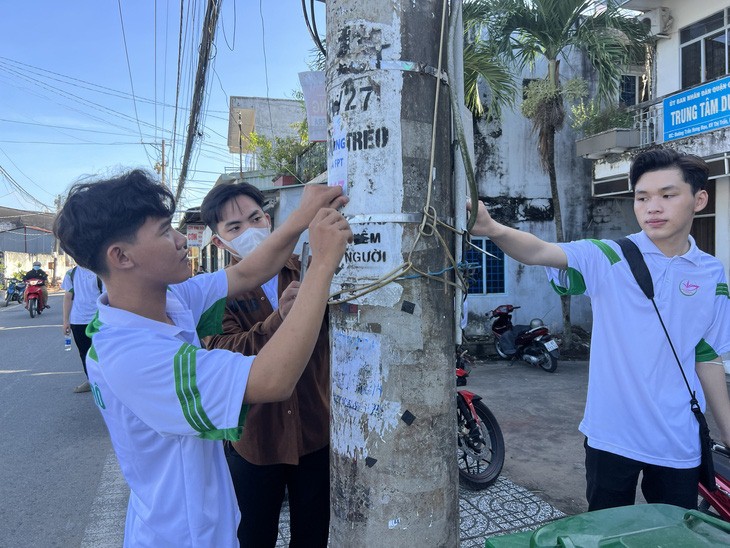 Young men remove advertisements stuck on a power pole in Cai Rang District, Can Tho City. Photo: Lan Ngoc / Tuoi Tre