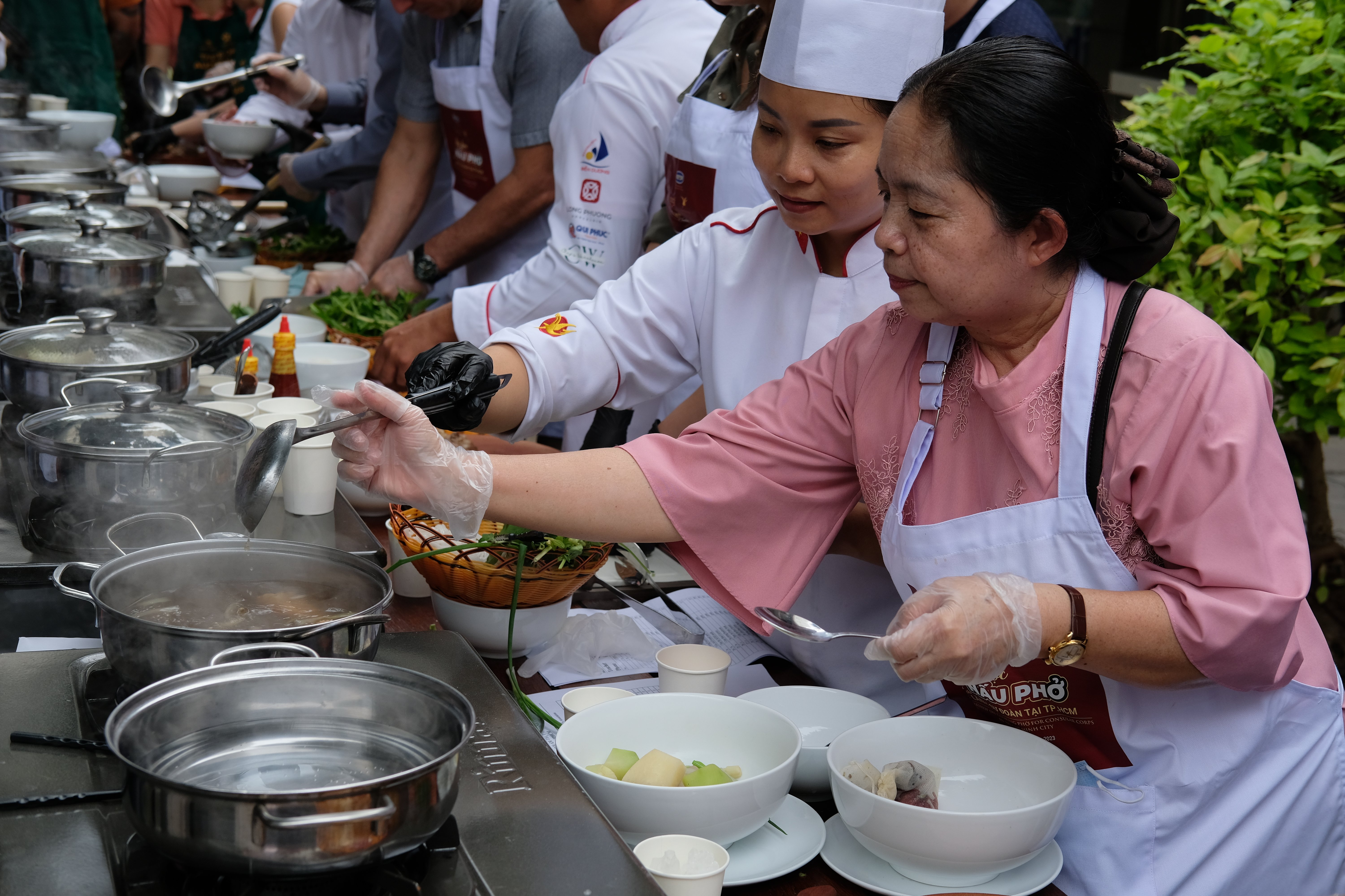A Vietnamese chef instructs a representative of the Consulate General of Cambodia (front) to cook pho at the pho cooking workshop for consular corps in Ho Chi Minh City on November 24, 2023. Photo: Tran Phuong / Tuoi Tre News
