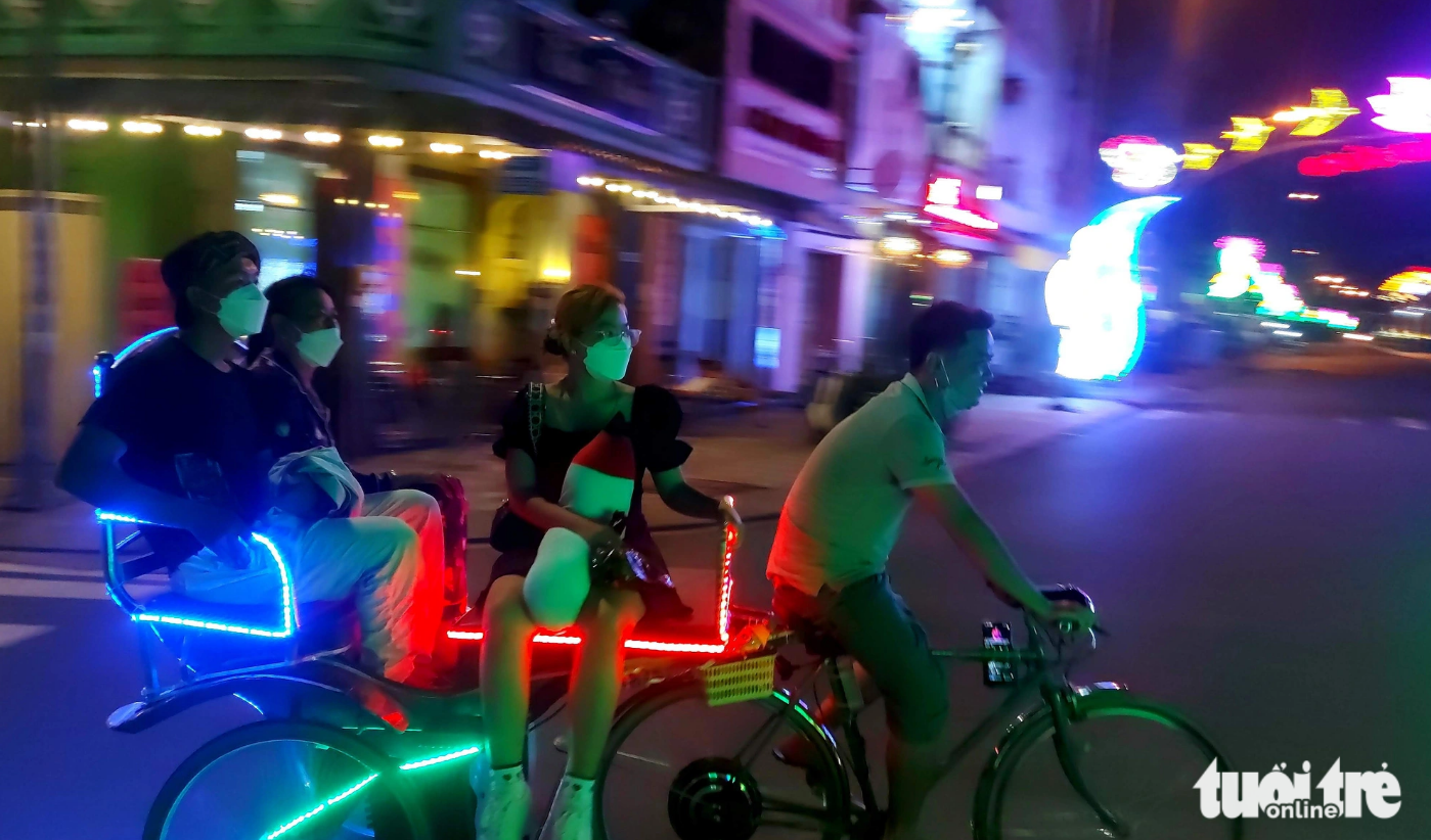 Travelers on an electric three-wheeled motorcycle take a look around Ha Tien City at night. Photo: Chi Cong / Tuoi Tre