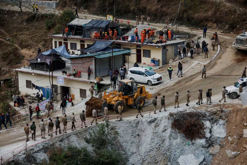 Policemen walk past a bulldozer as it lays down mud to flatten a road outside the tunnel where operations are underway to rescue trapped workers, after a tunnel collapsed in Uttarkashi in the northern state of Uttarakhand, India, November 28, 2023. Photo: Reuters