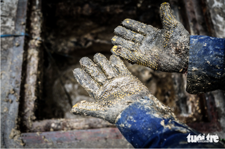 A drainage worker’s hands are full of waste oil and grease after he emerges from a sewer. Photo: Phuong Quyen / Tuoi Tre