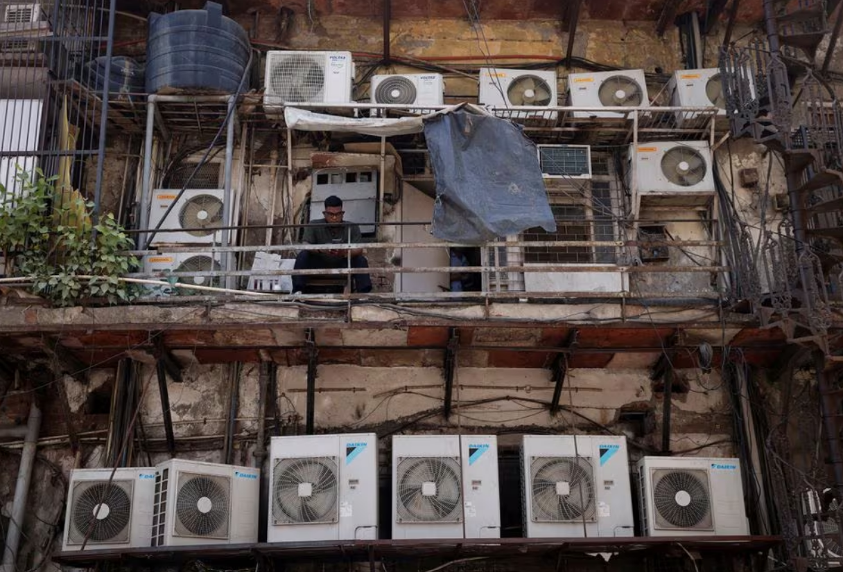A man uses his mobile phone as he sits amidst the outer units of air conditioners, at the rear of a commercial building in New Delhi, India, April 30, 2022. Photo: Reuters