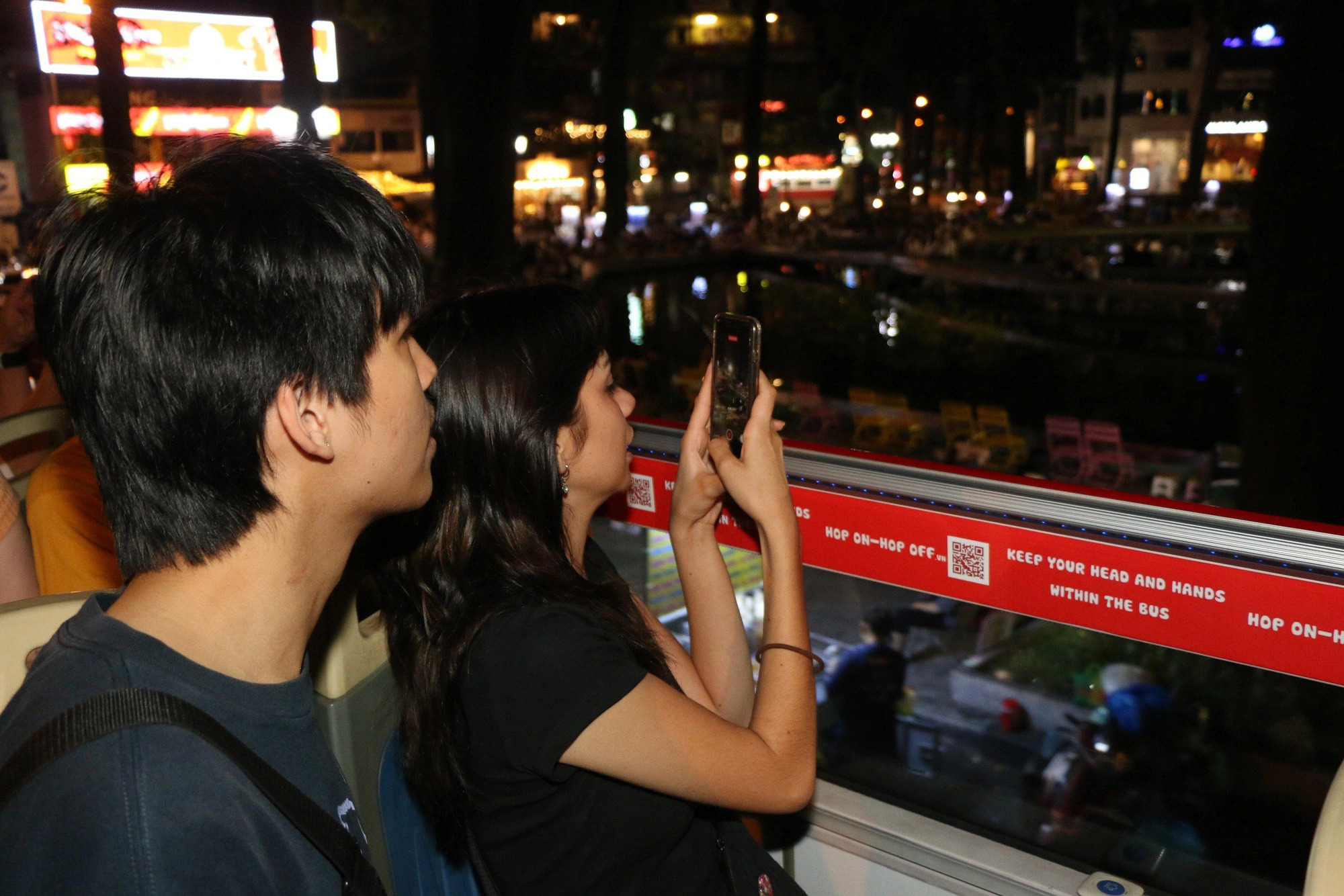 Two visitors explore Ho Chi Minh City at night on a double-decker bus. Photo: K.L / Tuoi Tre