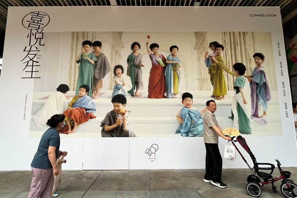 A man pushes a stroller and a woman holds a child as they walk past a billboard in Shenzhen, Guangdong province, China April 21, 2023. Photo: Reuters