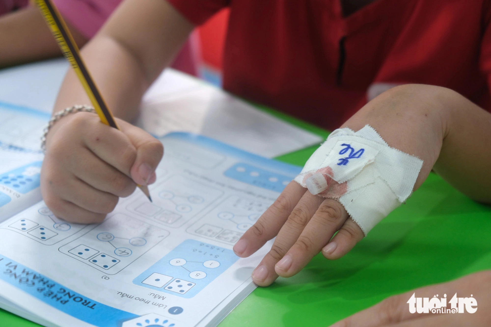 A child patient with an infusion needle on the hand is practicing writing in a ‘happy class’. Photo: Ngoc Phuong / Tuoi Tre