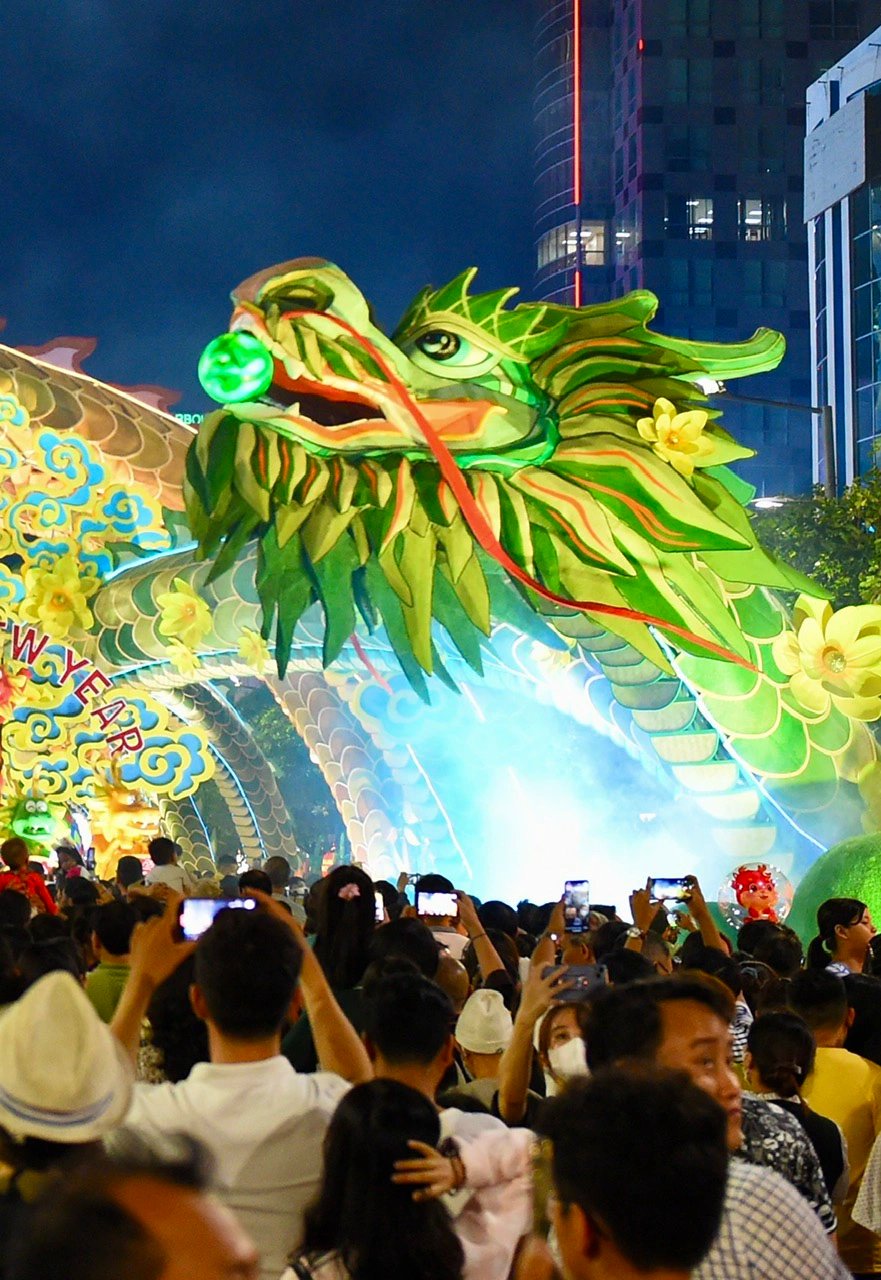 Visitors use their phones to check out a flying dragon in augmented reality through an app provided by the organizers while visiting the Nguyen Hue Flower Street in District 1, Ho Chi Minh City on its opening night on February 7, 2024. Photo: Tuoi Tre