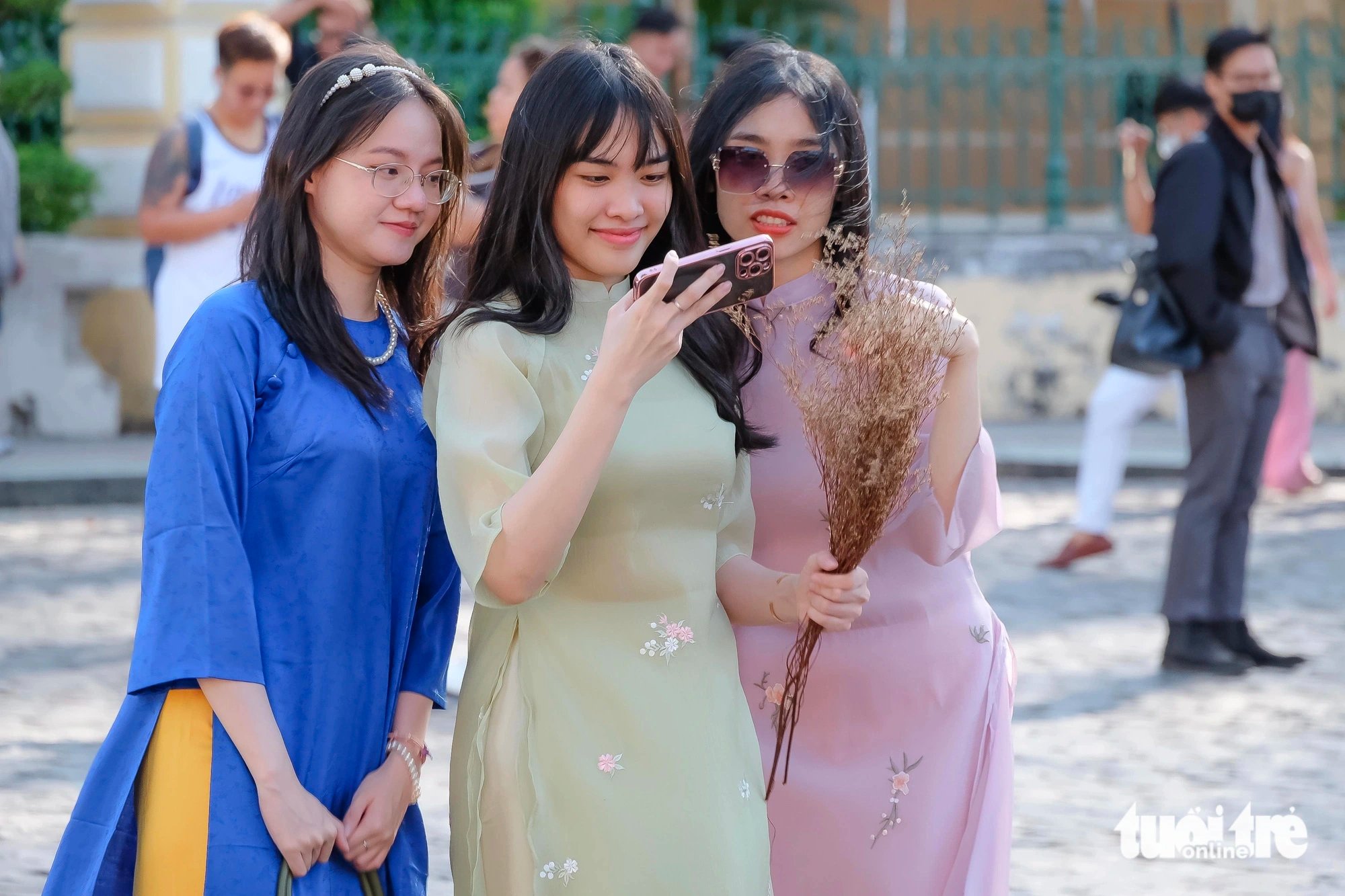 Three young ladies check their phones after taking a photo in front of the Saigon Central Post Office in District 1, Ho Chi Minh City on February 11, 2024. Photo: Phuong Nhi / Tuoi Tre