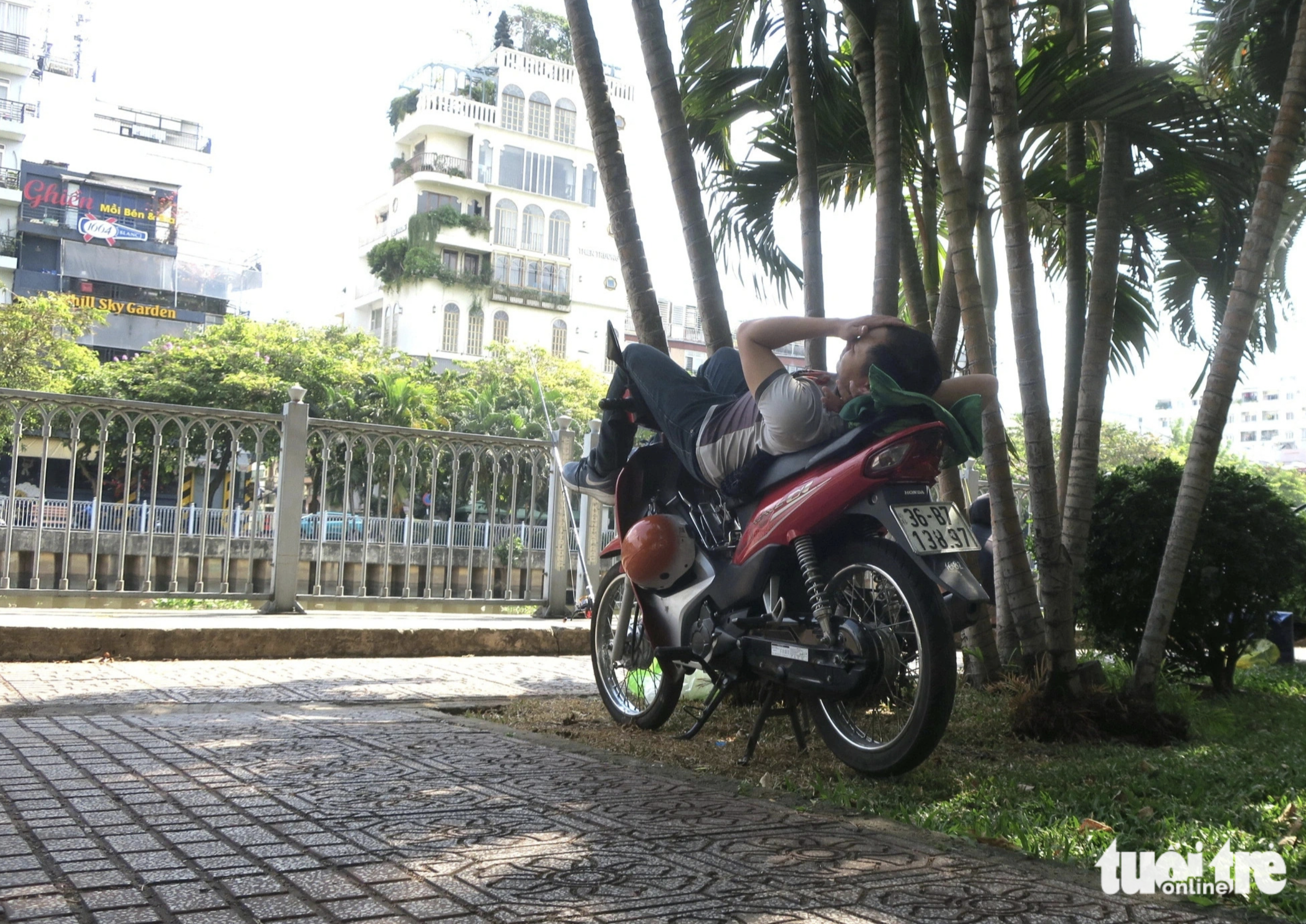 A man takes a nap on his motorbike in the shadow of trees near a canal along Hoang Sa Street, Phu Nhuan District, Ho Chi Minh City. Photo: T.T.D. / Tuoi Tre
