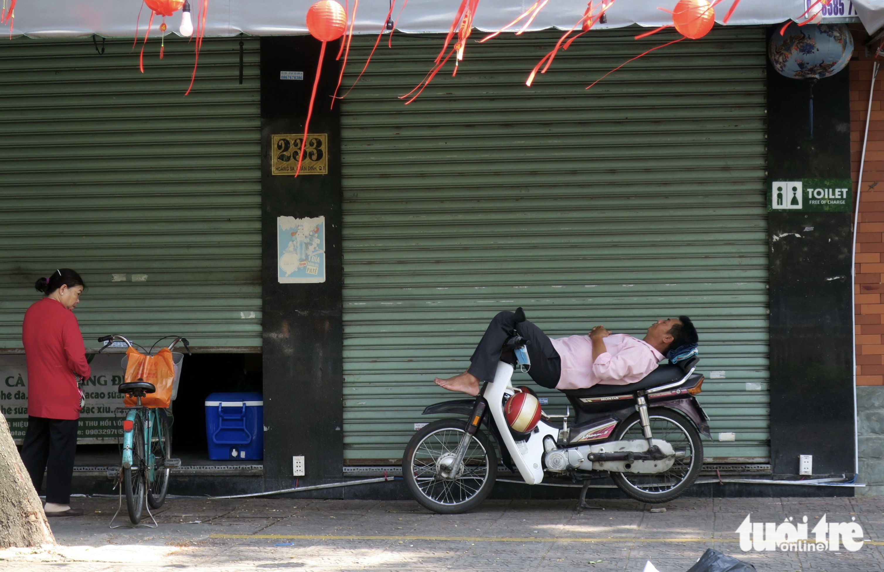 A motorcycle taxi driver takes a rest on his motorcycle in the shade of a house roof on Truong Sa Street in District 1. Photo: T.T.D. / Tuoi Tre