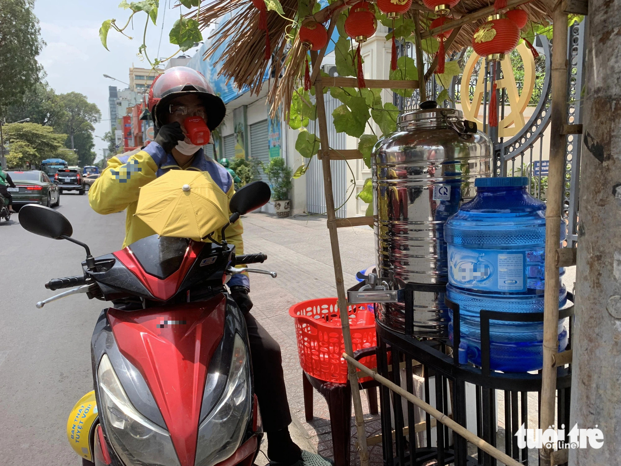 A motorbike ride-hailing drivers drinks from vine-shaded charity water tanks outside a church on Nguyen Thi Minh Khai Street in District 1, Ho Chi Minh City. Photo: Hien Anh / Tuoi Tre