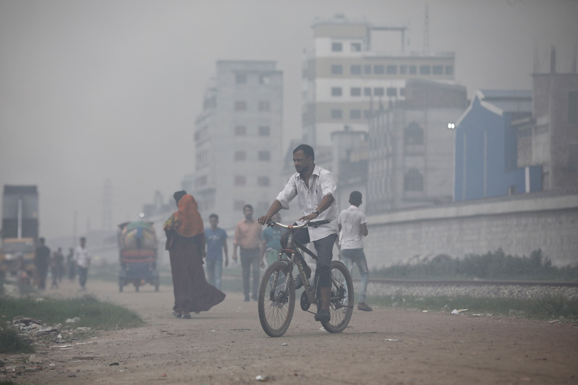 A man rides a bicycle through smoke rising from steel mills located near a slum in Dhaka, Bangladesh August 29, 2023. Photo: Reuters
