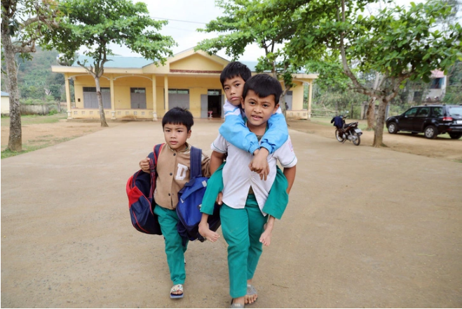 In Vietnam, student gives friend piggyback rides, another carries their schoolbags to class
