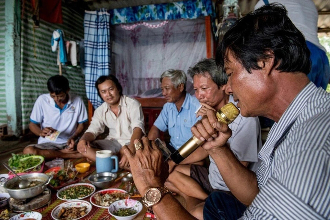 A man (R) sings karaoke while a group of other men sit around a large spread of food in a residential home. Photo: AFP
