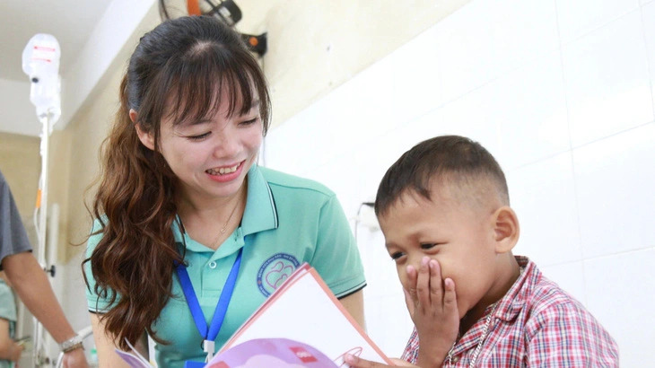 Tran Cao Thanh Binh (L), head of Social Work Department at the Da Nang Hospital for Women and Children in Da Nang City, gives a coloring book for a young cancer patient named ALang Hai Quan (R). Photo: Doan Nhan / Tuoi Tre