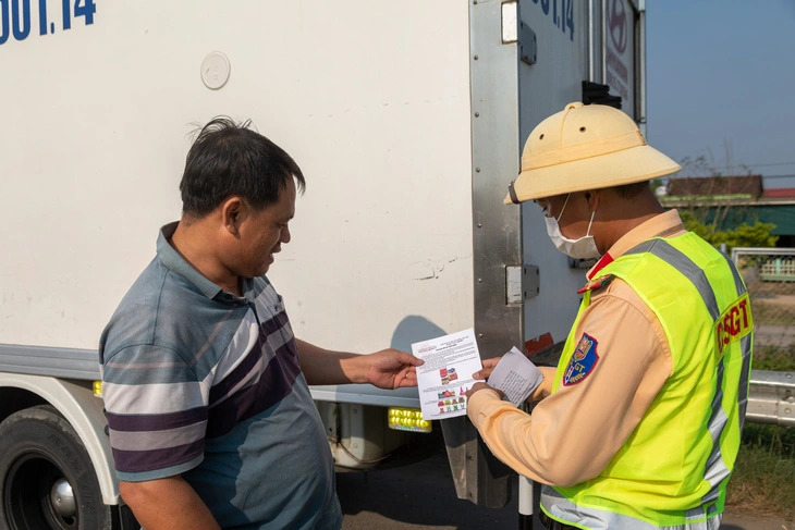 A traffic police officer hands a driver a leaflet instructing how to handle traffic incidents on the Cam Lo - La Son thruway that links Thua Thien - Hue and Quang Tri Provinces. Photo: Hoang Tao / Tuoi Tre