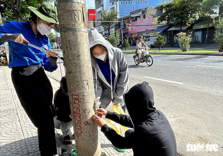 Young people remove ads from a utility pole in Da Nang City, located in central Vietnam. Photo: Doan Nhan / Tuoi Tre