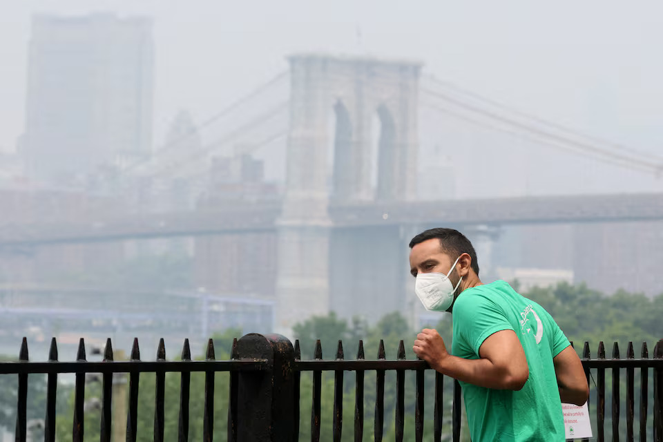 A man wears a mask while looking at lower Manhattan shrouded in haze and smoke from wildfires in Canada from the Brooklyn Promenade in New York City, U.S., June 30, 2023.  Photo: Reuters