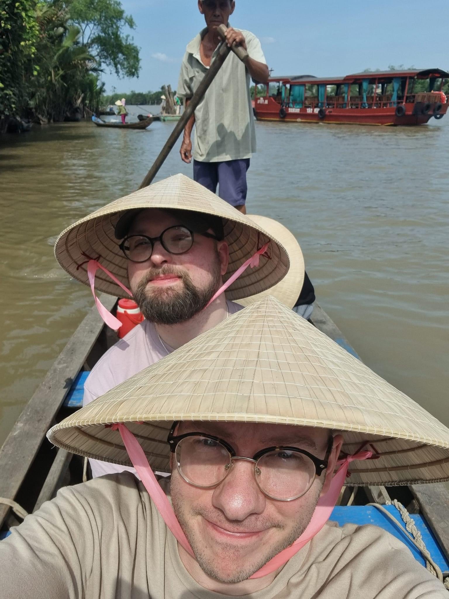 Calum Dalton (front) and his husband wear nón lá (Vietnamese conical hats) on a boat trip in Vietnam’s Mekong Delta. Photo: Supplied