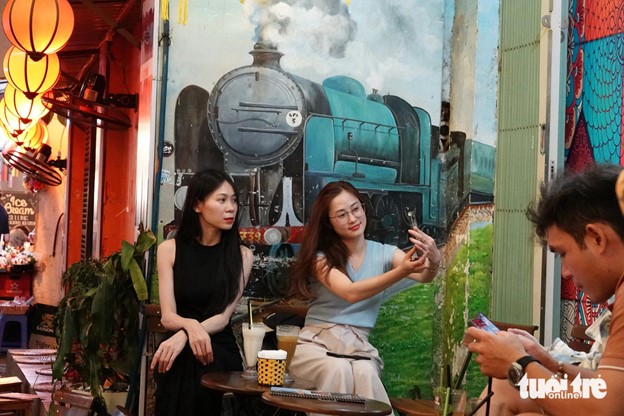 Two tourists take photos with a painting of a train on a wall. Photo: T.T.D. / Tuoi Tre