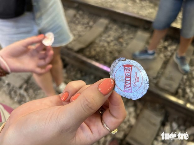 Foreign visitors hold beer bottle caps which are flattened by trains. Photo: T.T.D. / Tuoi Tre