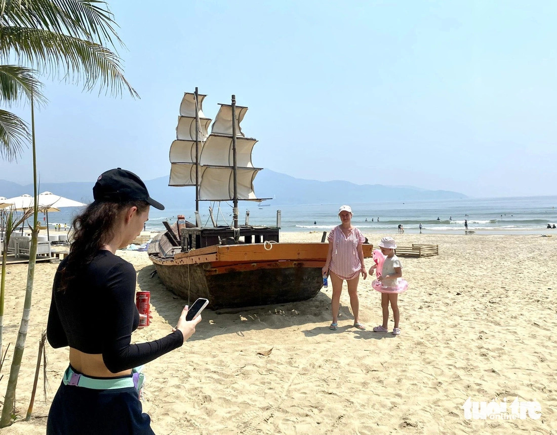 Russian visitors pose for a photo near a sailboat on the My Khe Beach in Da Nang City, central Vietnam on April 27, 2024. Photo: Truong Trung / Tuoi Tre