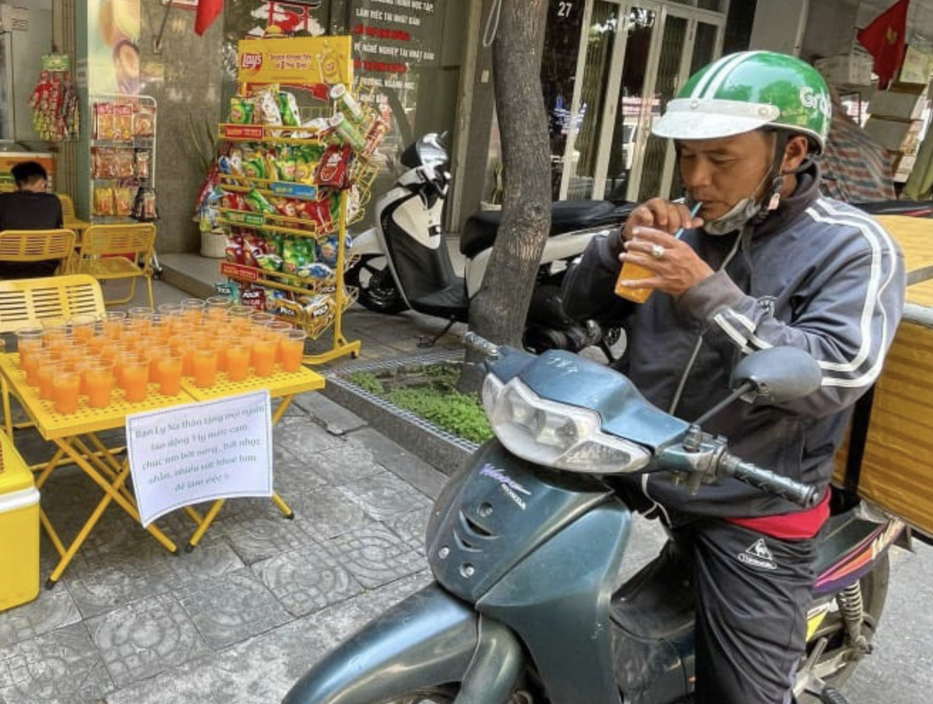 A delivery worker stops to drink a free glass of orange juice in front of a store in Da Nang City