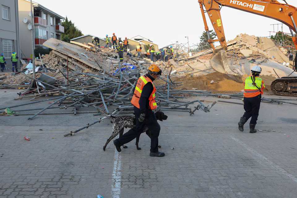 A rescue worker walks with a dog past the site where construction workers are trapped under a building that collapsed in George, South Africa May 7, 2024. Photo: Reuters