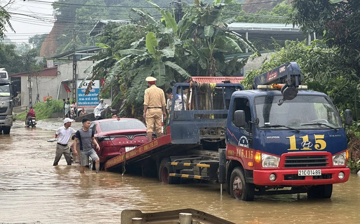 A traffic police officer and several men help take a broken-down car onto a rescue truck on a flooded road. Photo: Y.Bai