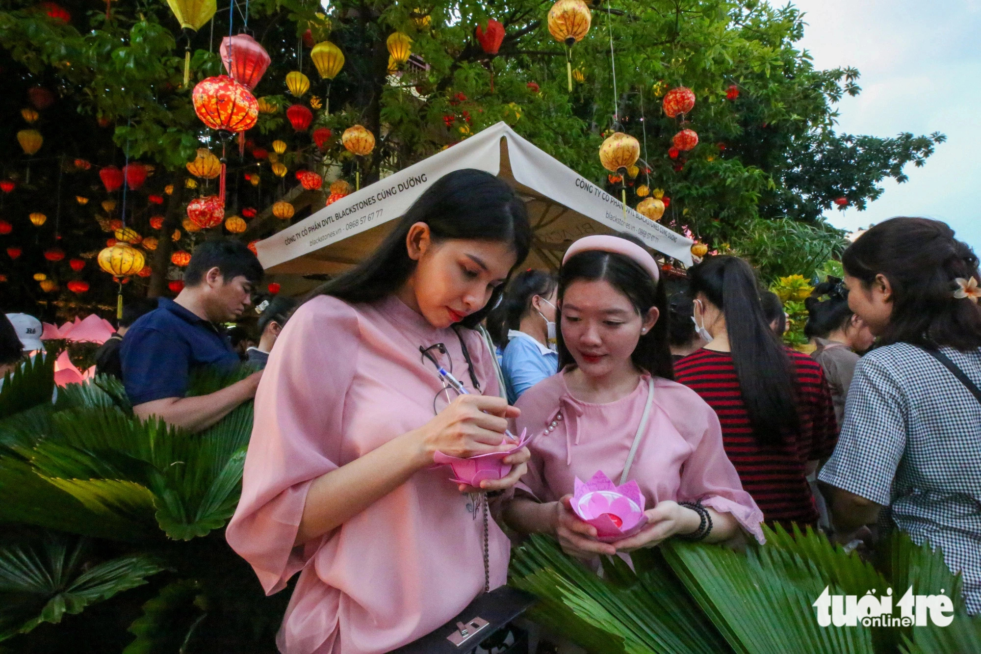Anh Thu (L) and her friend from District 10, Ho Chi Minh City come to the Phap Hoa Pagoda area early to find a perfect spot for releasing water lanterns. Photo: Phuong Quyen / Tuoi Tre