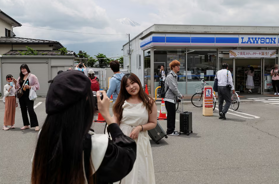 A tourist poses for a photo of Mount Fuji appearing over a convenience store after a barrier to block the popular tourist spot was installed, in Fujikawaguchiko town, Yamanashi prefecture, Japan, May 21, 2024. Photo: Reuters