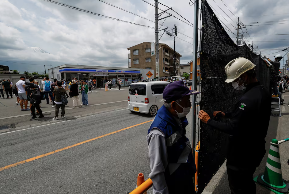 Tourists stand nearby as workers erect a barrier to block the view of a popular Mount Fuji photo spot, near a convenience store in Fujikawaguchiko town, Yamanashi prefecture, Japan, May 21, 2024. Photo: Reuters
