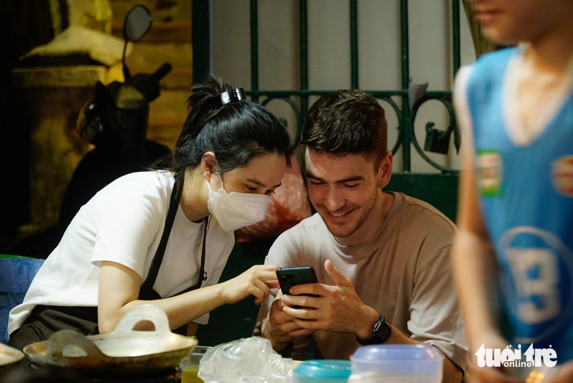 Moritz, a 28-year-old Swiss man, and his girlfriend, Le Duyen, watch a smartphone together at her eatery on Phan Dinh Phung Street in Hanoi. Photo: Nguyen Hien / Tuoi Tre