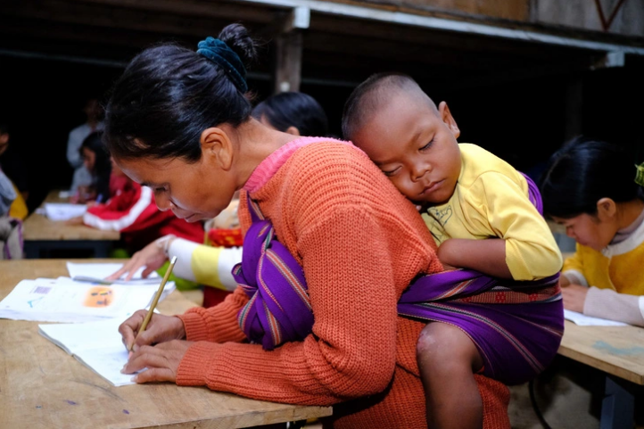 Duong, a 41-year-old member of the literacy class, practices writing while her four-year-old son sleeps on her back. Photo: T.Luc / Tuoi Tre