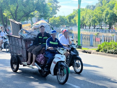 People sitting on a rudimentary garbage vehicle do not wear helmets.