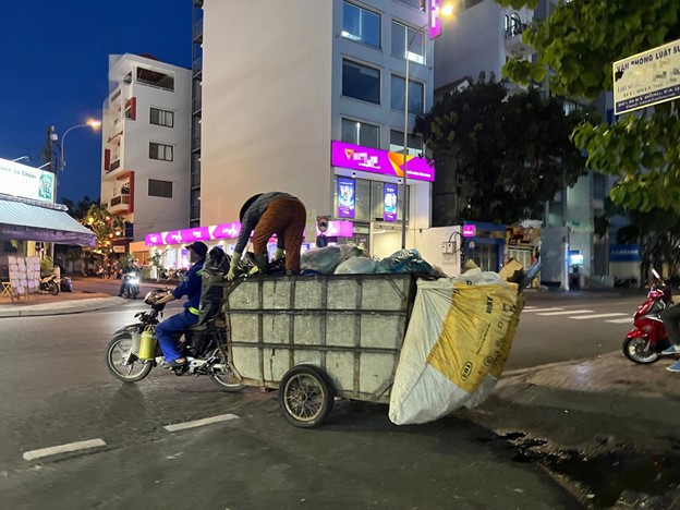 A woman presses garbage on a rudimentary vehicle while it is running.