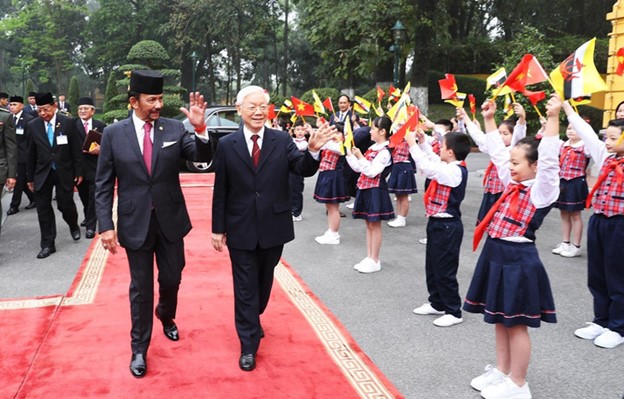 Sultan Haji Hassanal Bolkiah of Brunei Darussalam (L) and Vietnamese Party General Secretary Nguyen Phu Trong wave at Vietnamese children during the former’s visit to Vietnam in 2019. Photo: Vietnam News Agency